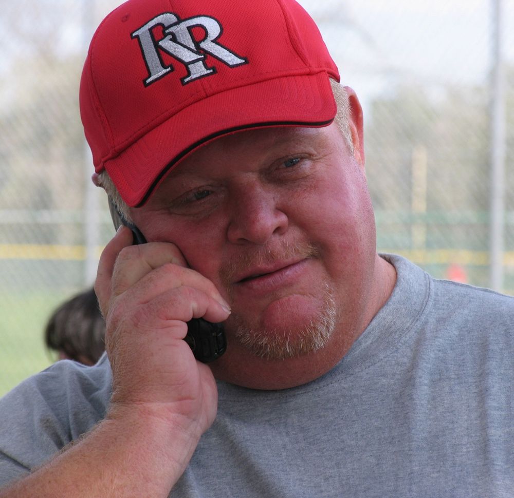 Coach Rick on the phone at the ballpark in his Red Raiders cap