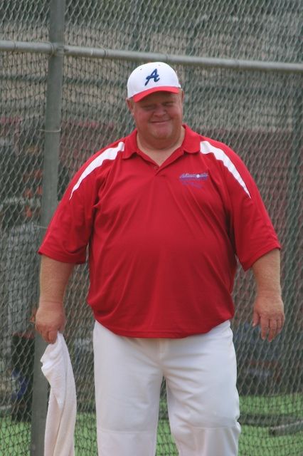 Coach Rick smiling in the dugout in an All Stars uniform